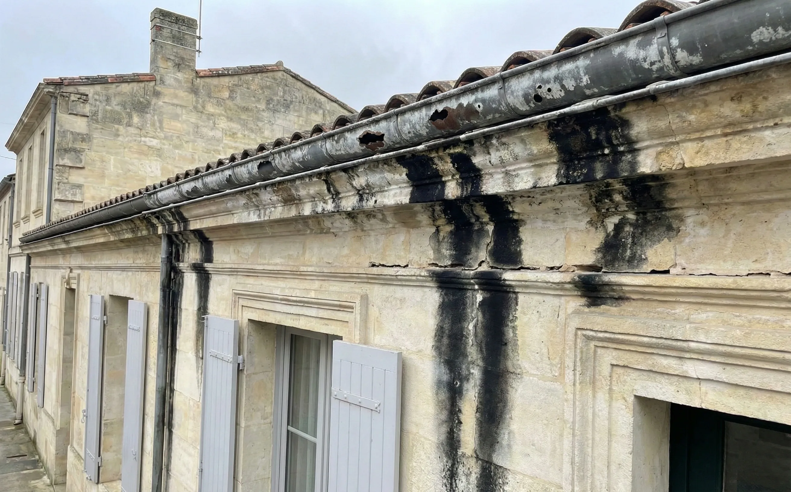 Façade en pierre calcaire XIXe avec traces noires de ruissellement sous gouttières zinc corrodées à Pessac-Centre