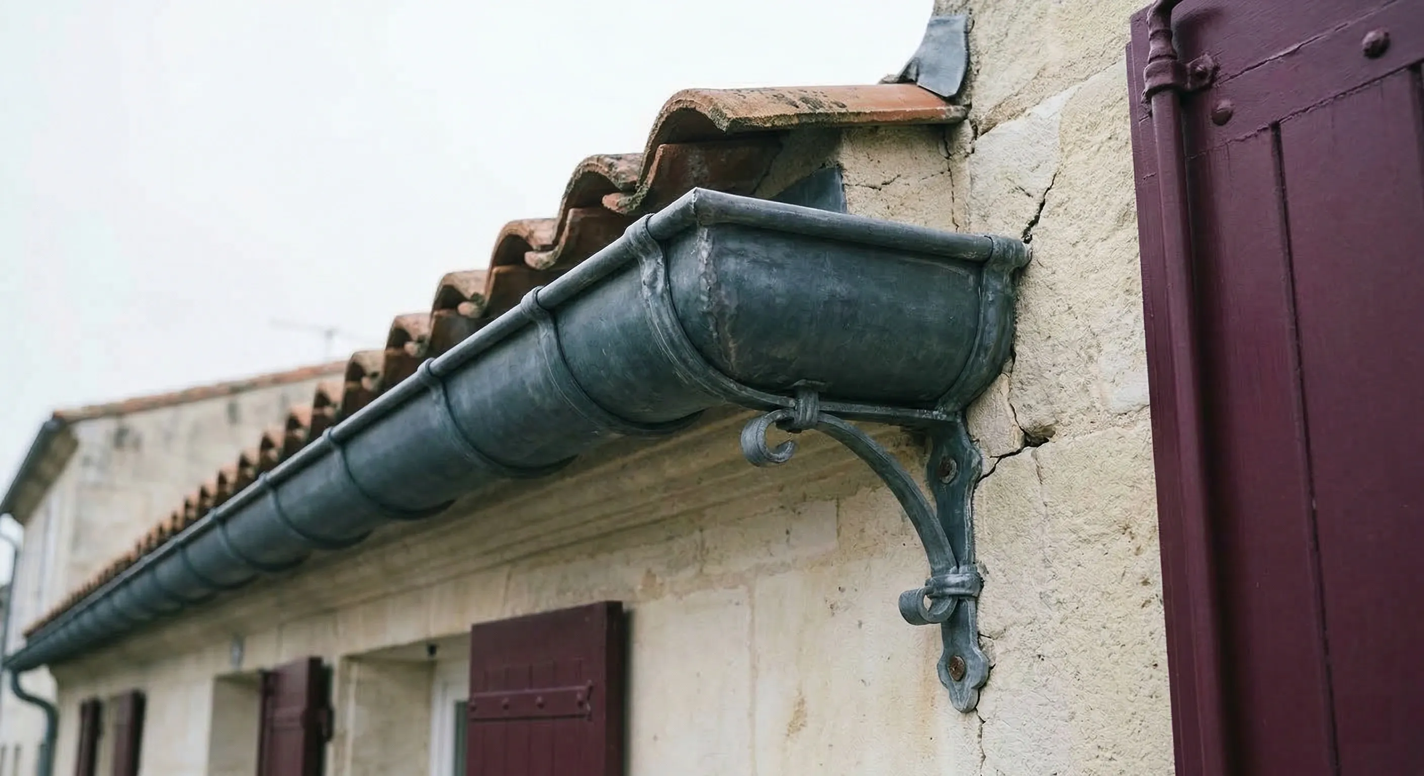 Gouttière moulurée nantaise en zinc sur une échoppe bordelaise à façade en pierre, rouleau décoratif et crochet ouvragé visibles