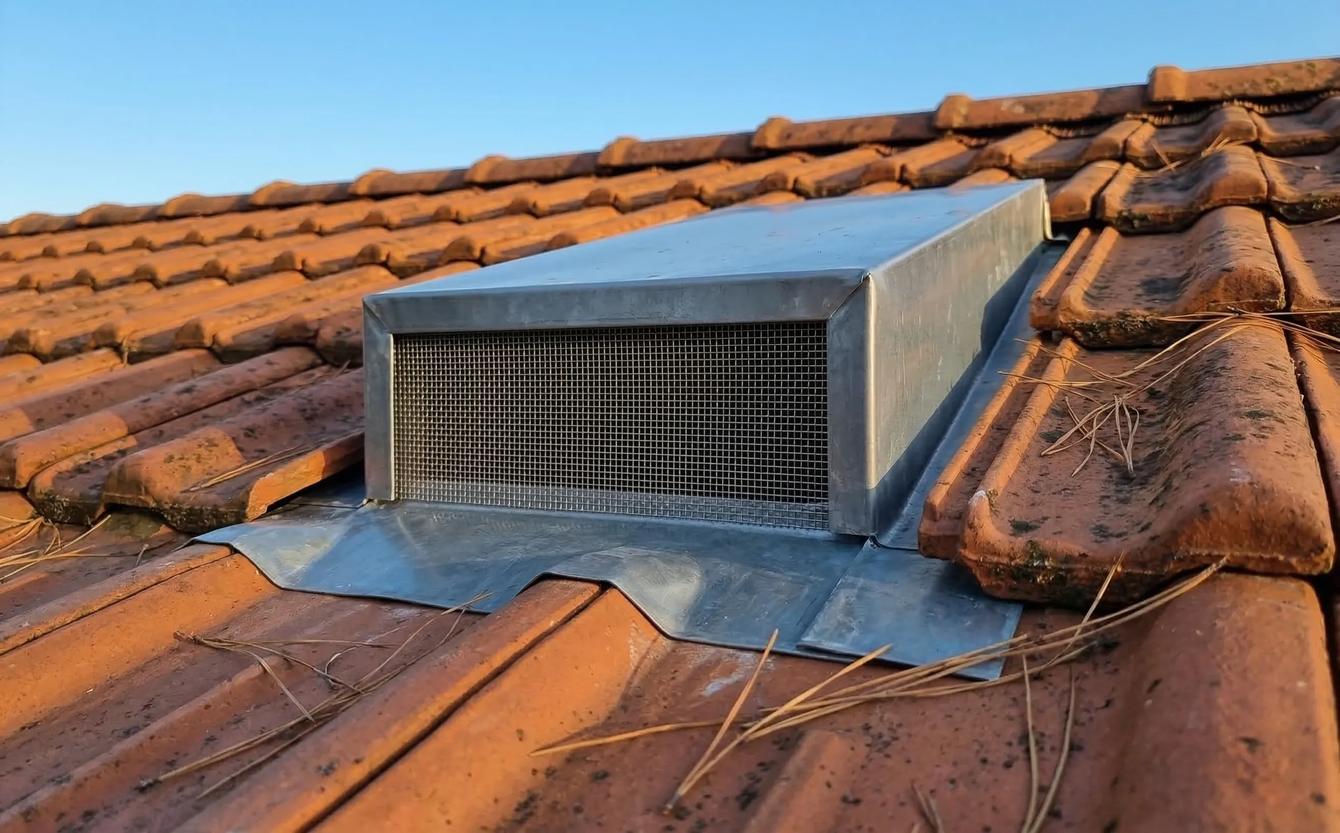 Grille anti-insectes à maille fine en inox posée sur une chatière de ventilation en zinc