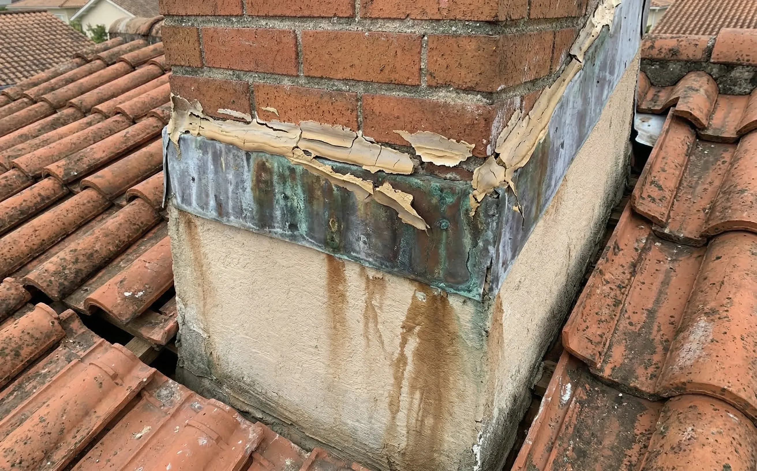 Ancien joint silicone fissuré et décollé autour d'une souche de cheminée avec traces d'humidité